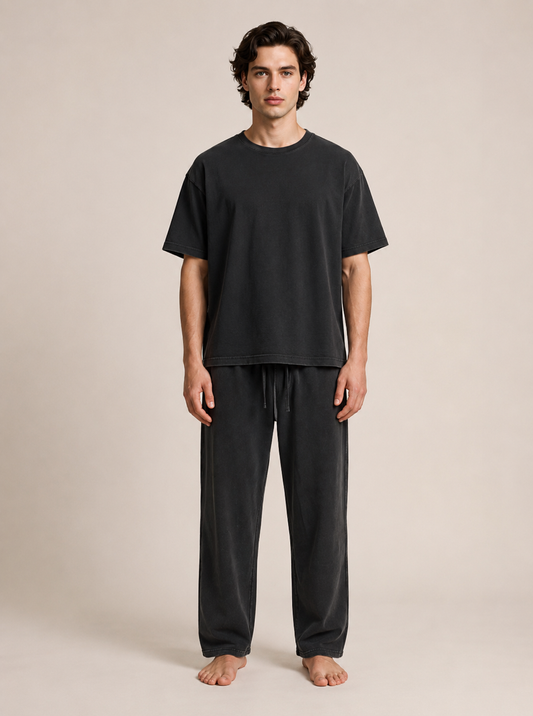 A man modeling a matching black short-sleeve t-shirt and drawstring sweatpants set against a plain beige studio background.