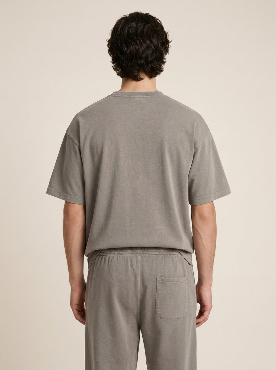 A man viewed from behind wearing a light gray short-sleeve t-shirt and matching gray lounge pants against a plain beige background.