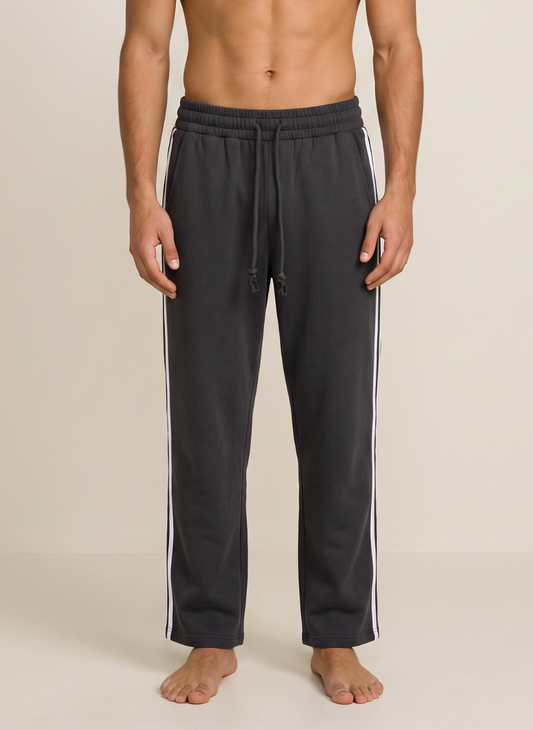 A man wearing dark charcoal gray sweatpants with white side stripes, shown from the waist down against a plain beige studio background.