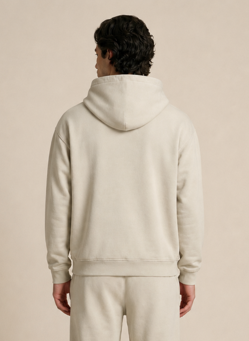 A man viewed from behind wearing a light cream-colored hoodie and matching sweatpants against a solid beige background.