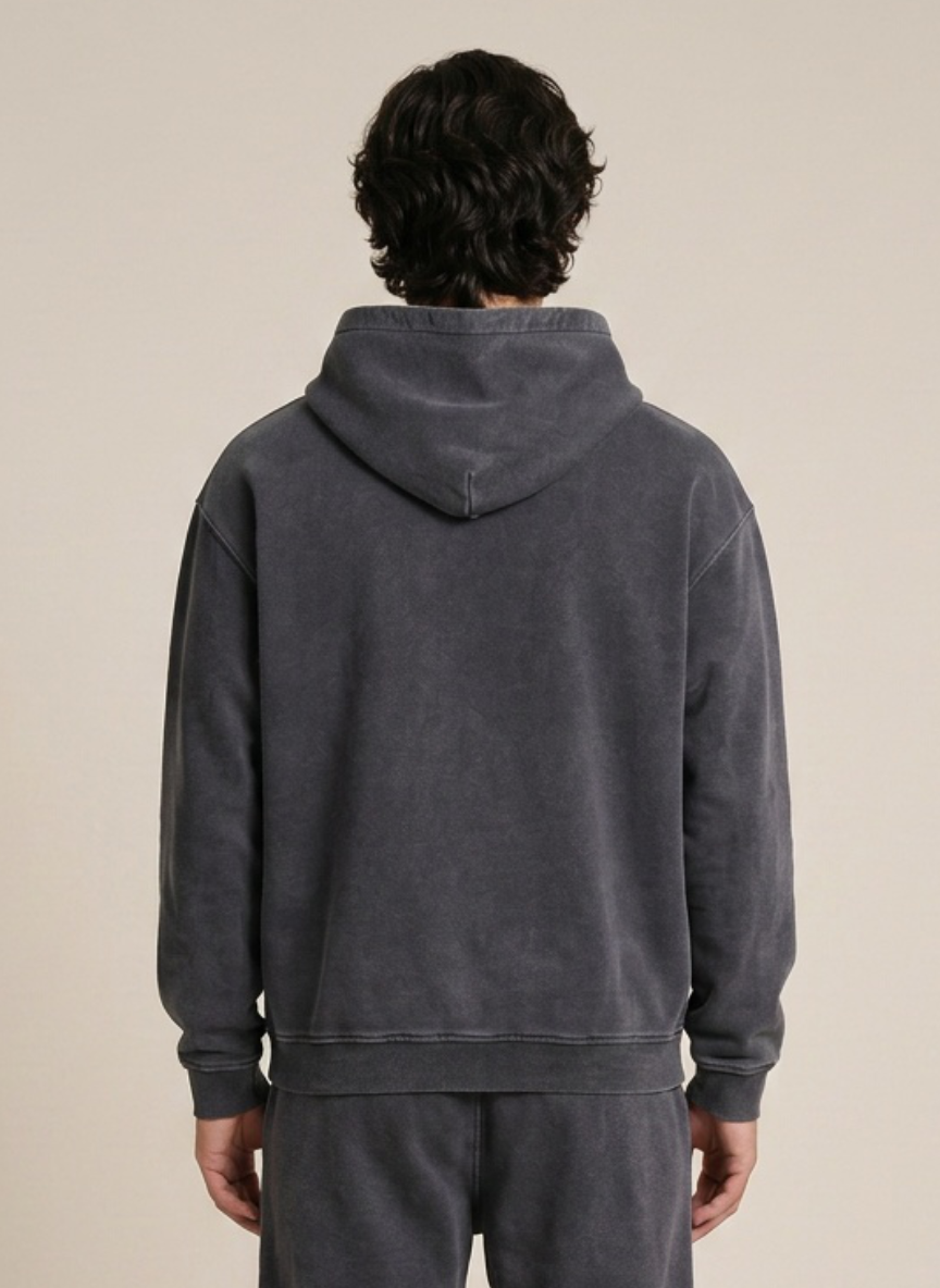 A person viewed from the back wearing a dark charcoal gray hooded sweatshirt and matching sweatpants against a plain beige studio background.