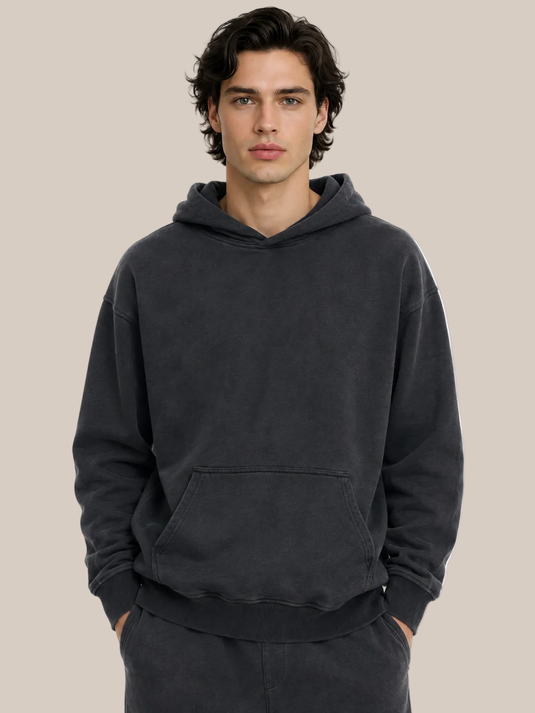 A man wearing a dark charcoal gray washed pullover hoodie with a front kangaroo pocket, shown from the chest down against a plain white background.