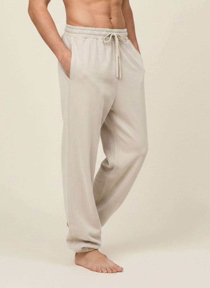 A man wearing light beige drawstring sweatpants, shown from the waist down against a plain beige studio background.