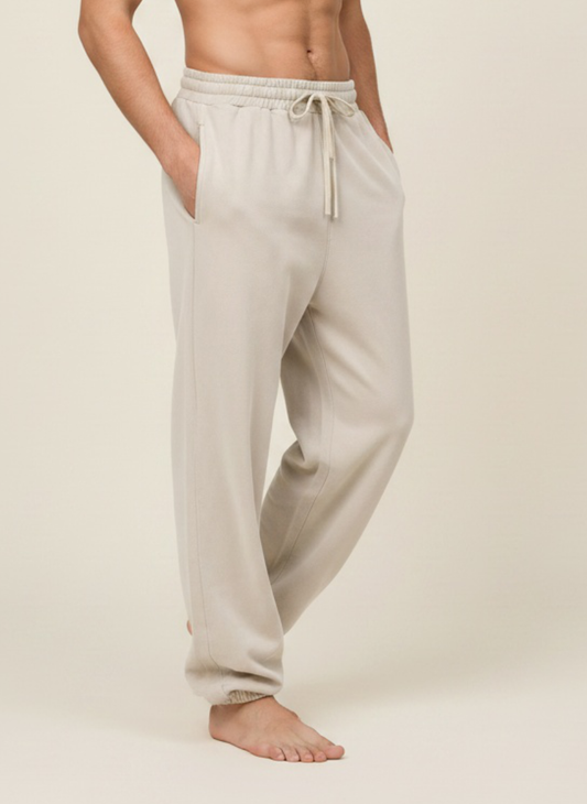 A man wearing light beige drawstring sweatpants, shown from the waist down against a plain beige studio background.