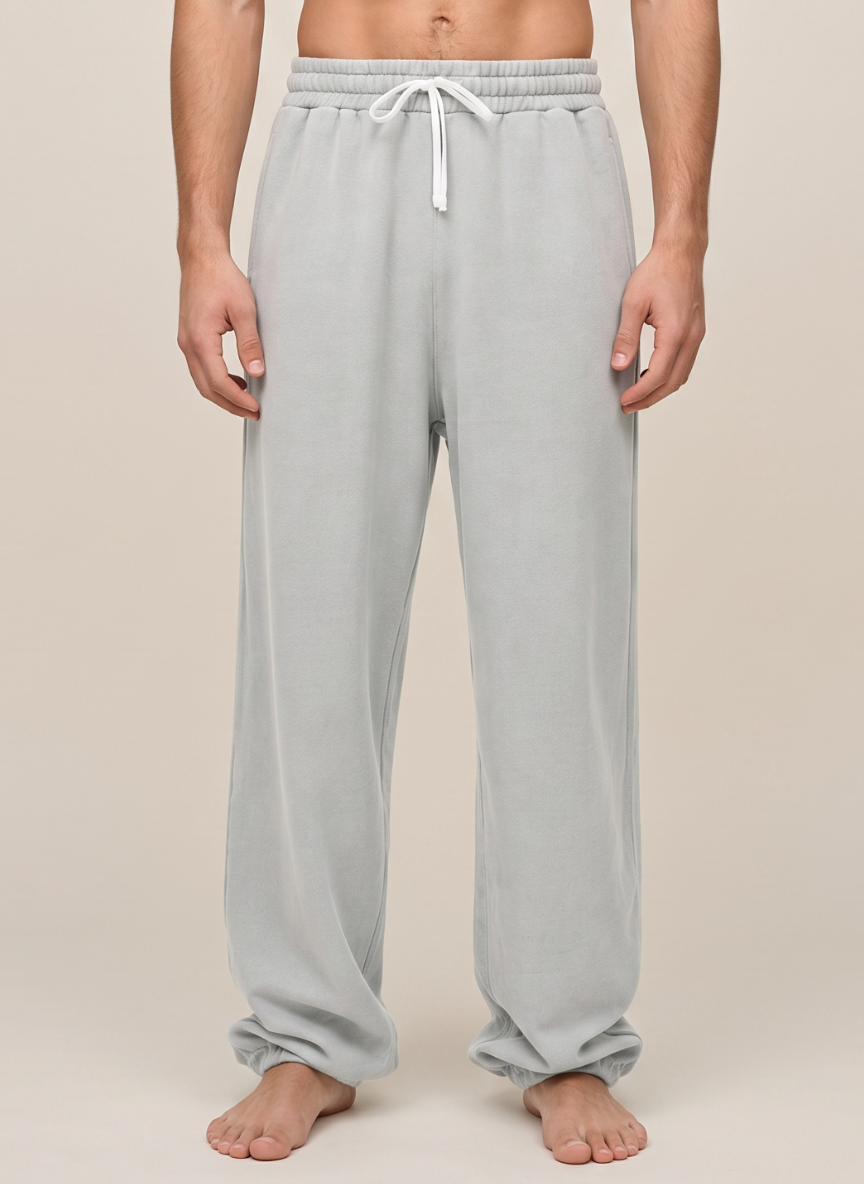 A person wearing light gray lounge pants with an elastic waistband and white drawstring, shown from the waist down against a plain beige studio background.