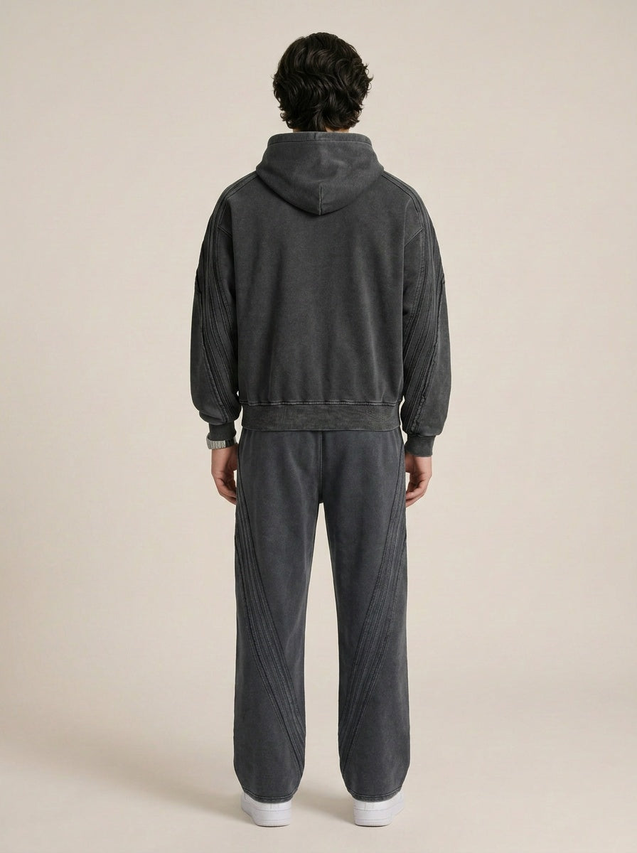 Backside of a model wearing a sun bleached deconstructed black hoodie with matching sweatpants on a beige background. 
