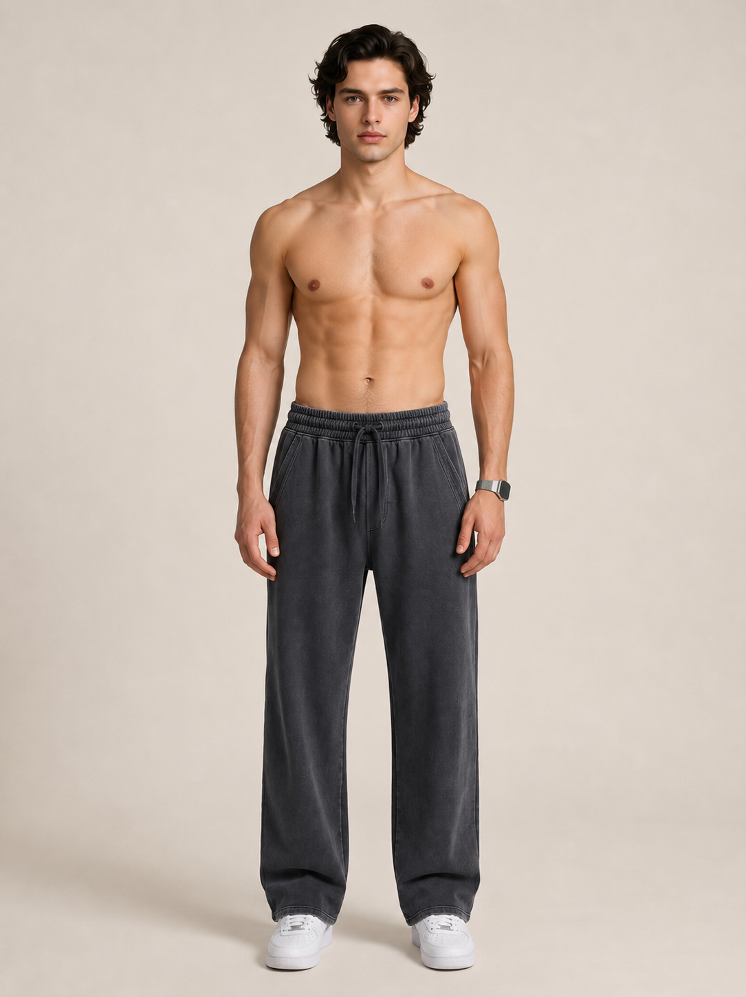 A model wearing a pair of black sweatpants on a beige background. 