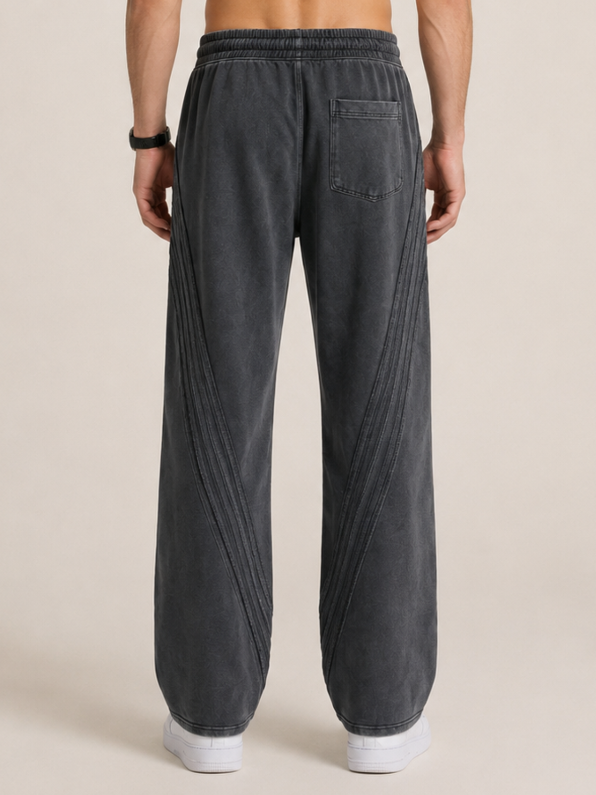 Backside close-up of a model wearing a pair of black sweatpants on a beige background. 