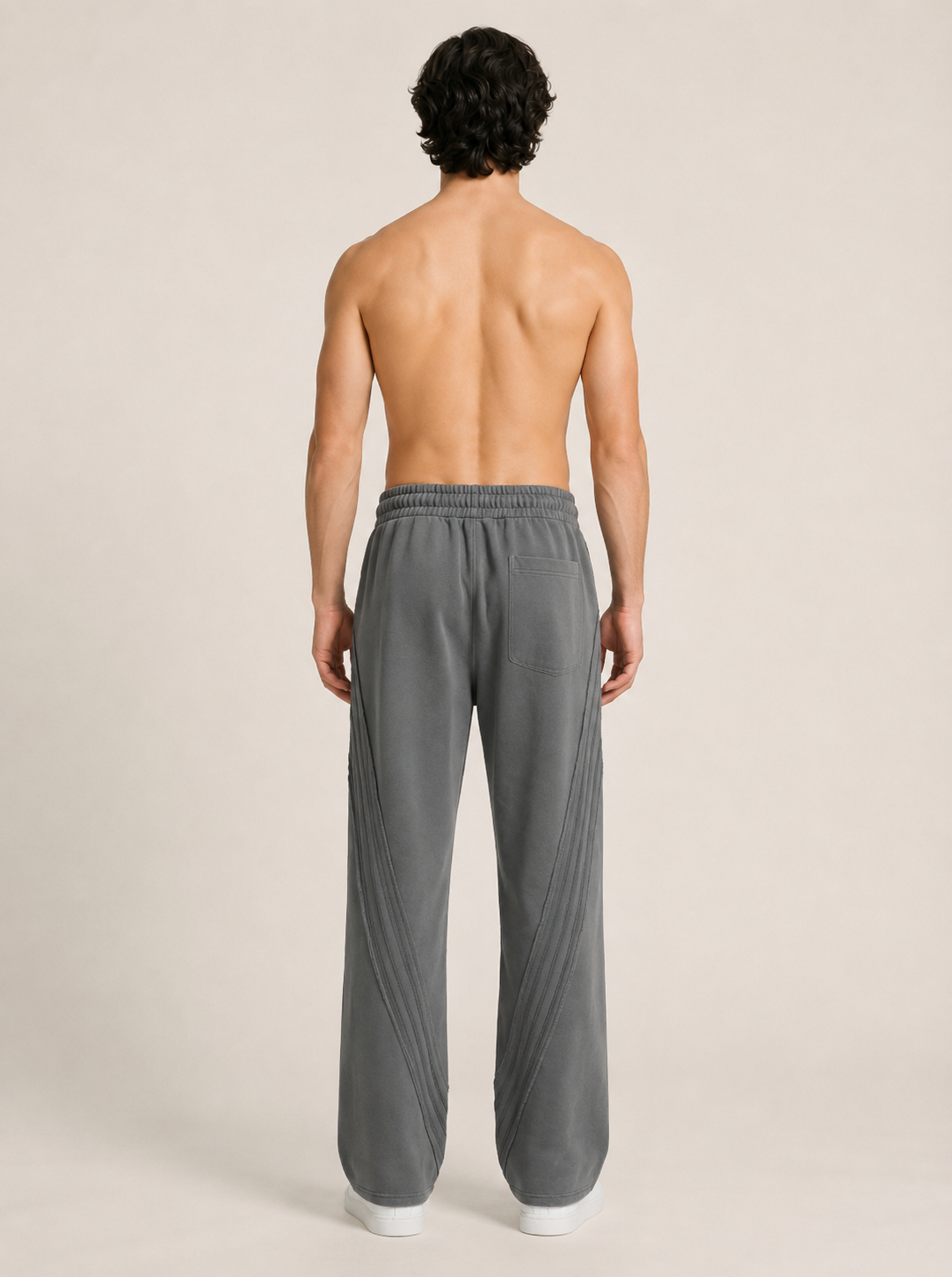 Full shot backside of a model wearing a pair of dark gray sweatpants on a beige background. 