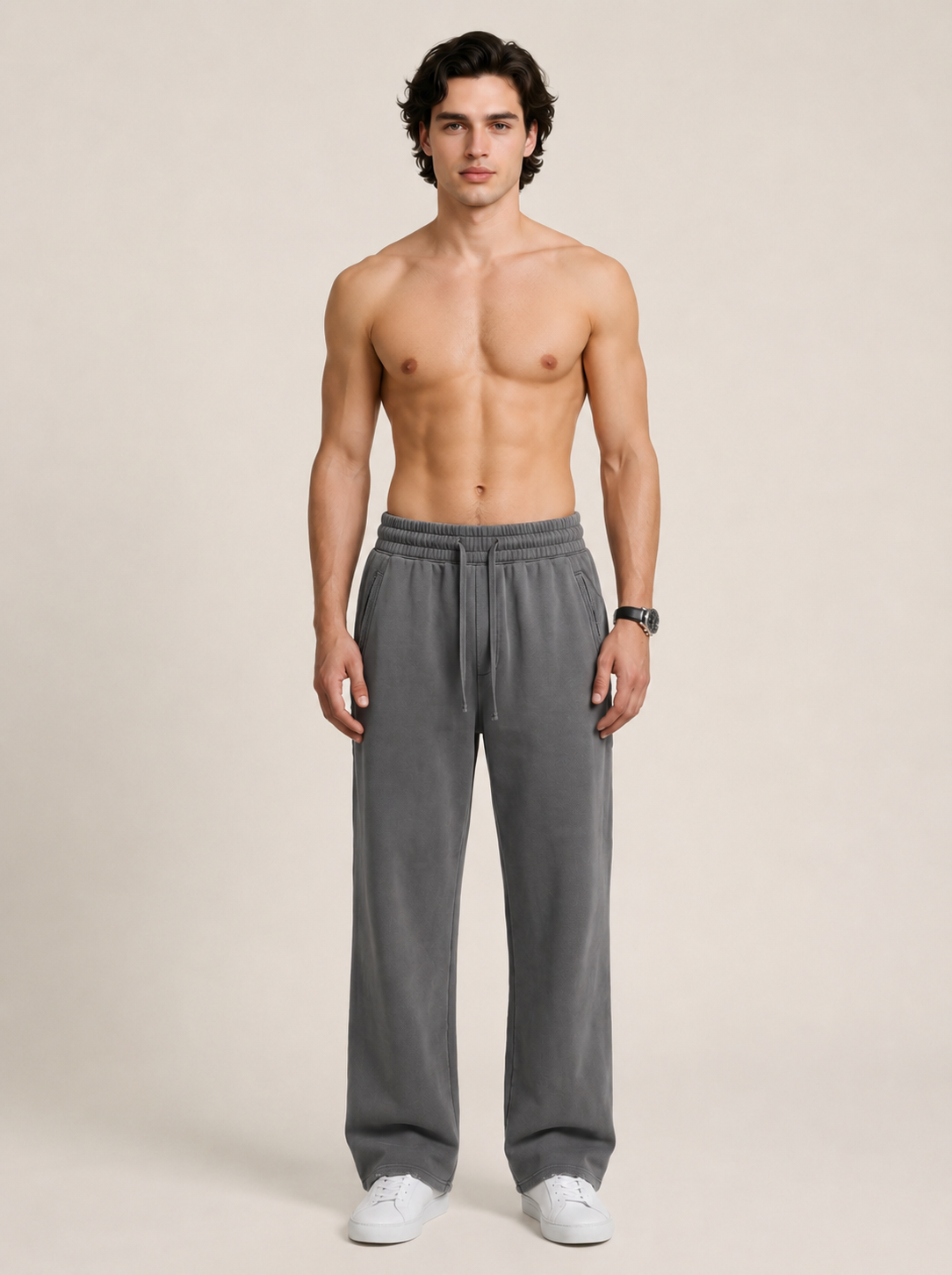 Full length shot of a model wearing a a pair of dark gray sweatpants on a beige background. 