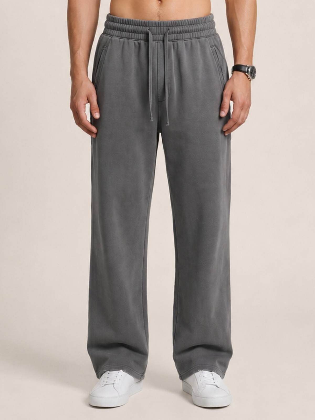 Close-up of a model wearing a pair of dark gray sweatpants on a beige background. 