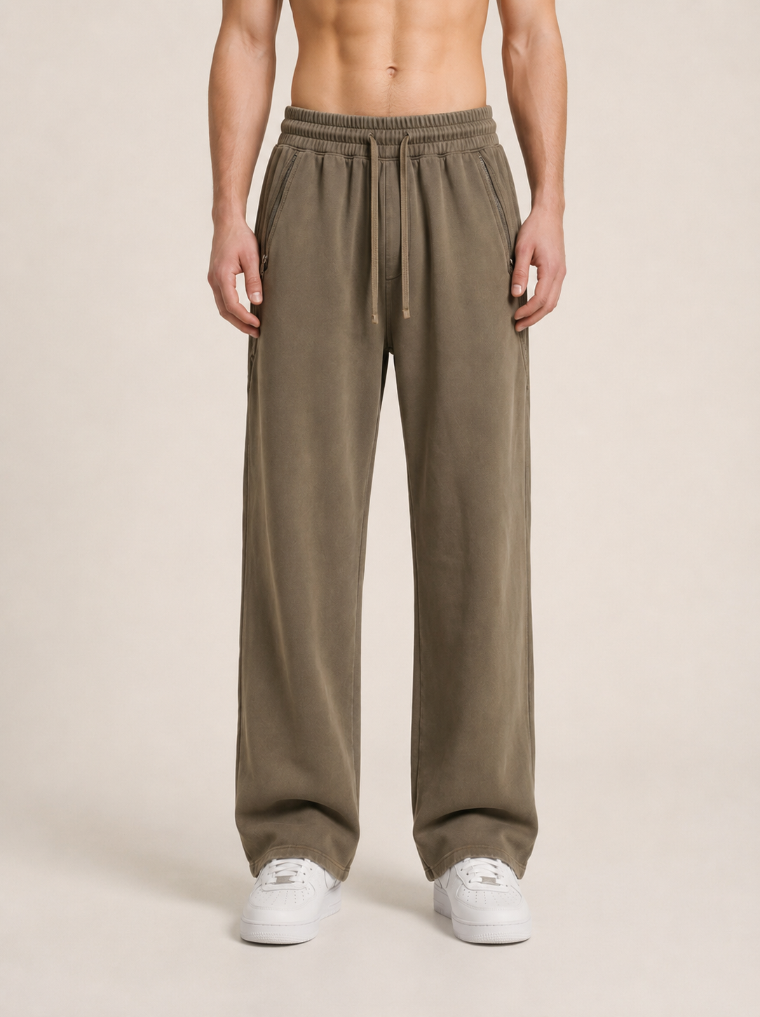 Close-up of a model wearing a pair of khaki sweatpants on a beige background. 