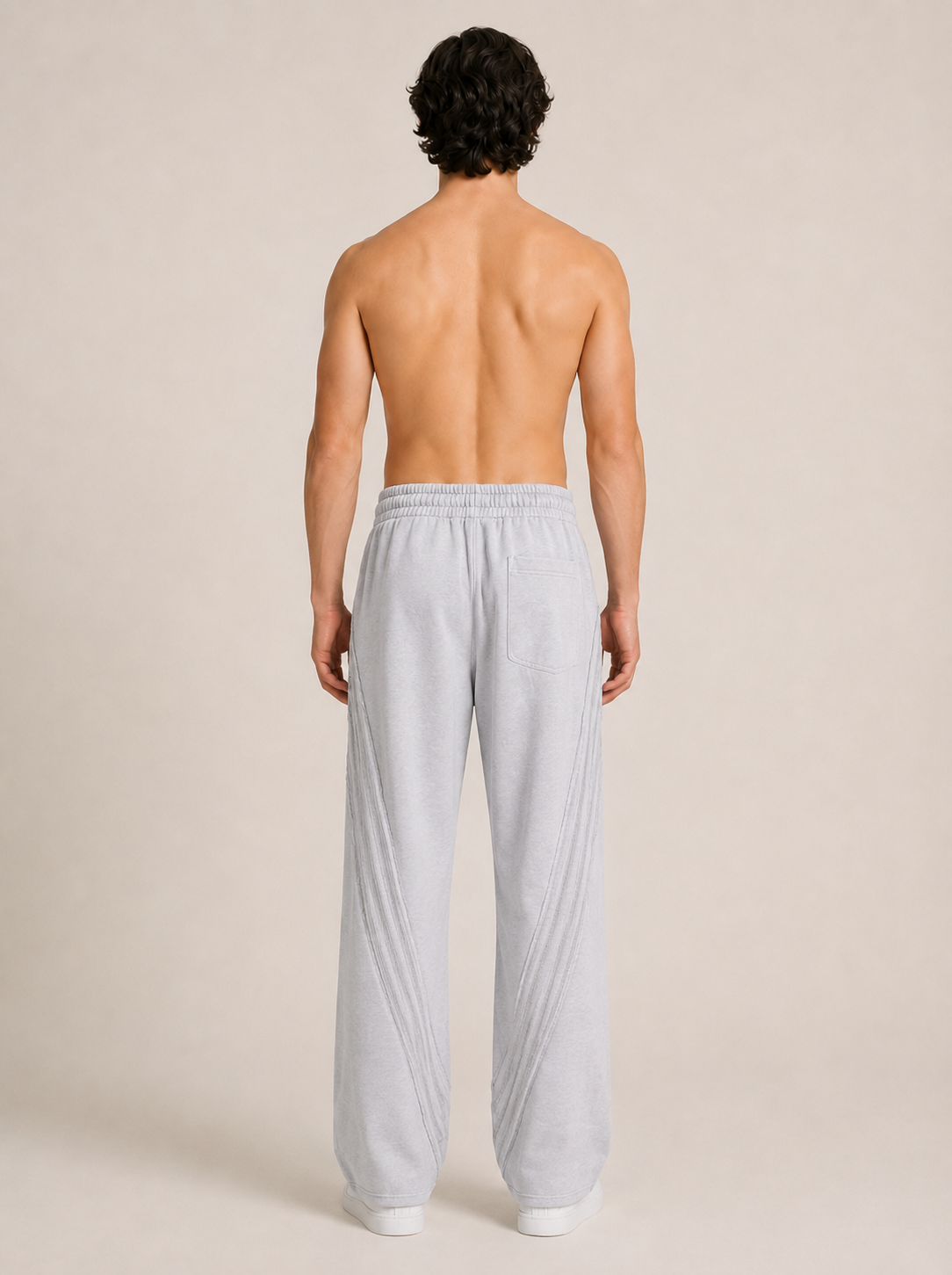 Full length backside shot of a model wearing a light gray pair of sweatpants on a beige background. 