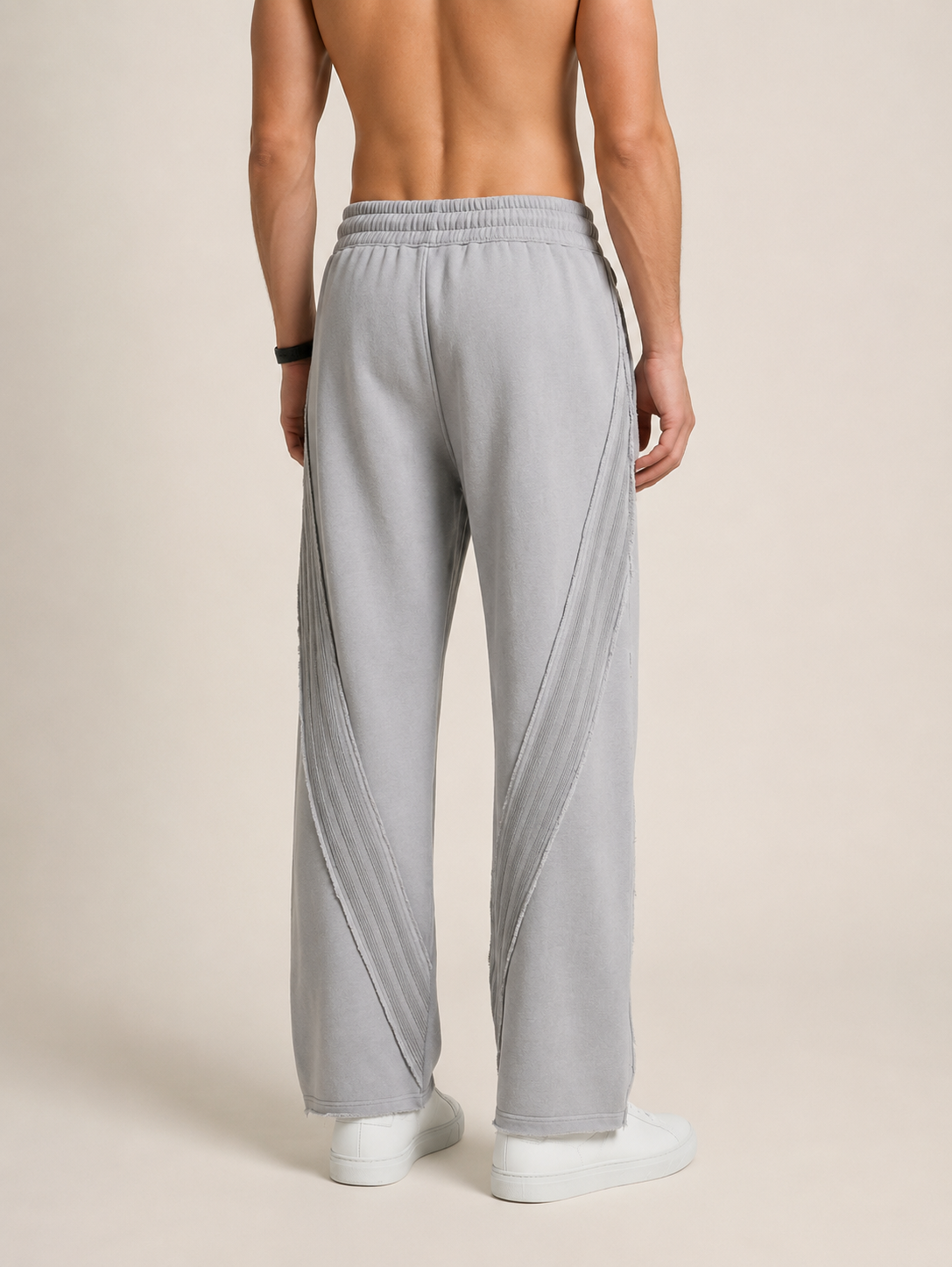 Backside close-up of a model wearing a pair of light gray sweatpants on a beige background. 