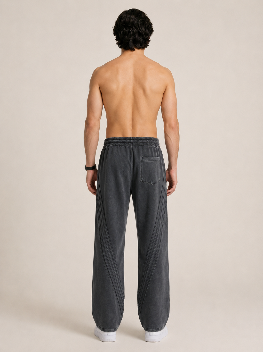 Full length backside shot of a model wearing a pair of black sweatpants on a beige background. 