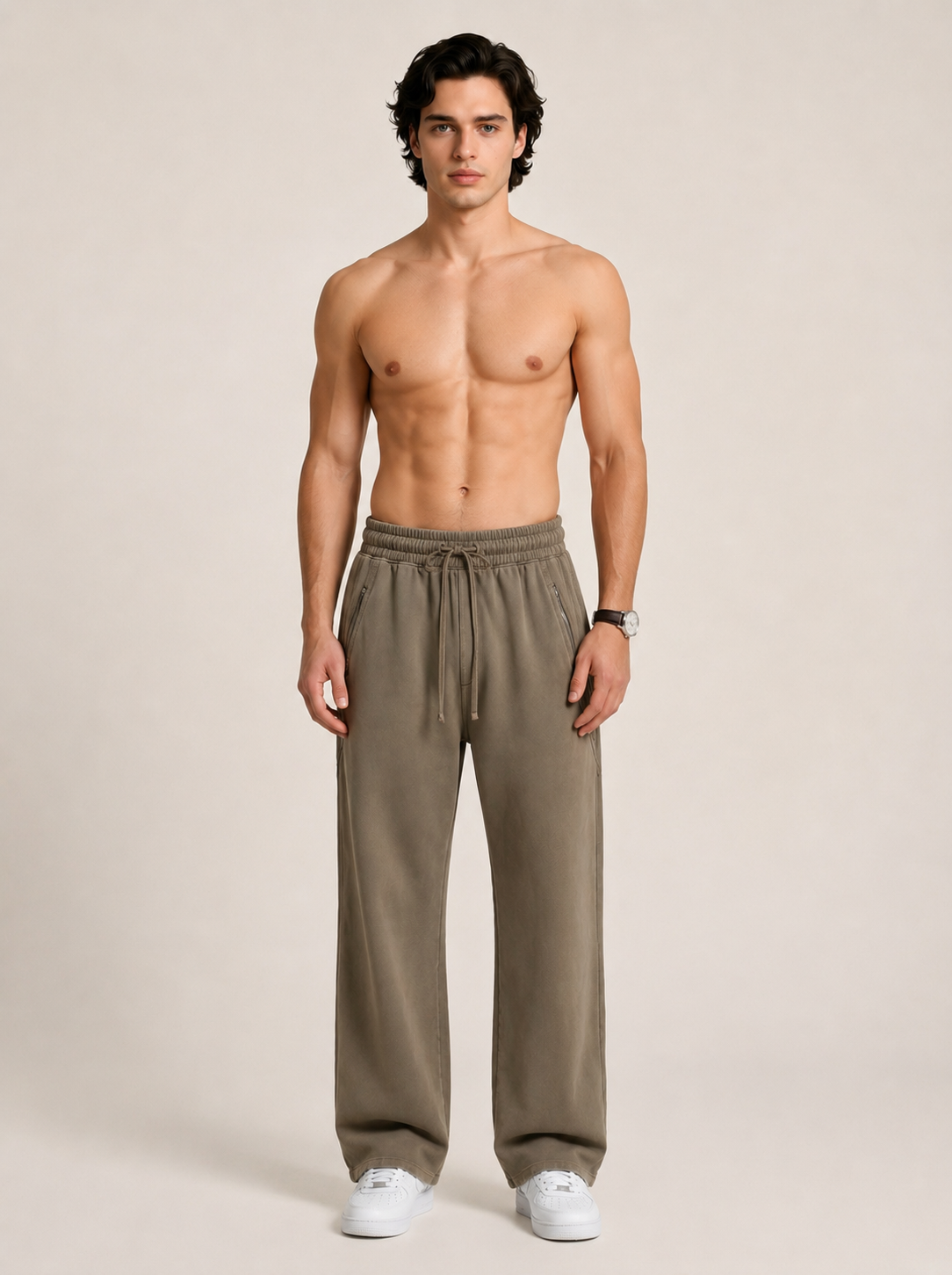 A model wearing a pair of khaki sweatpants on a beige background. 