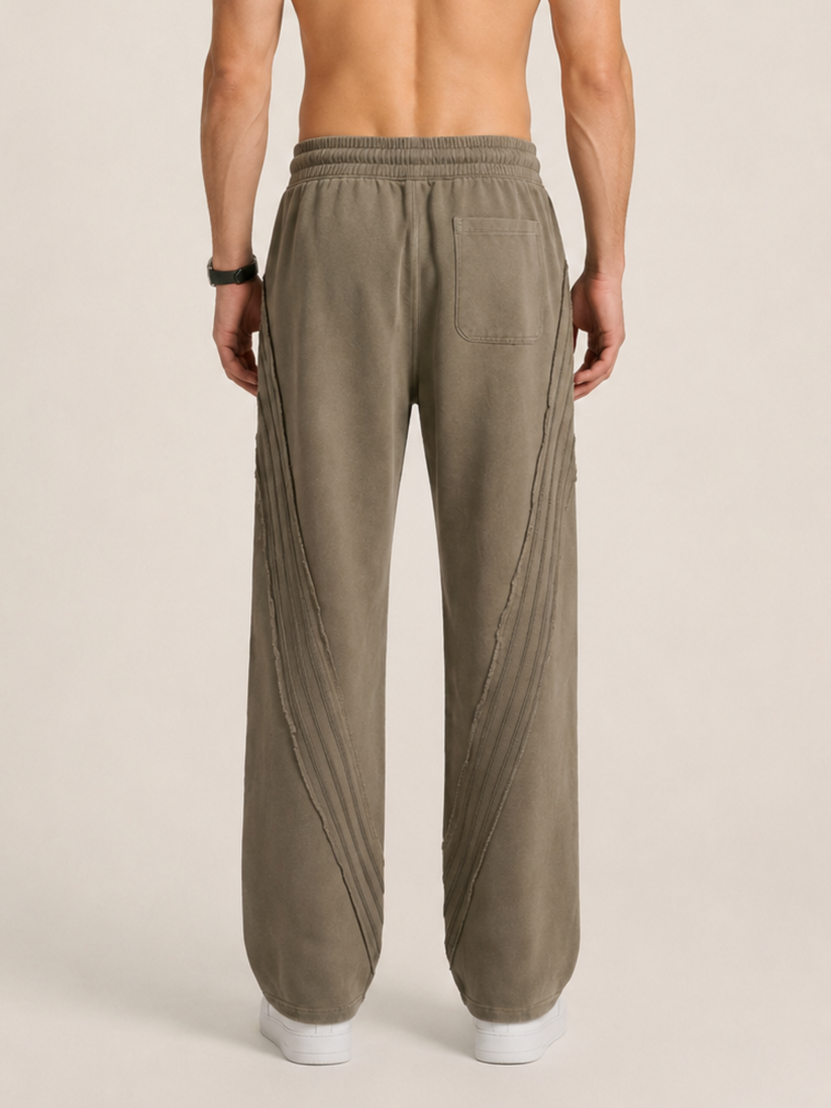 Backside close-up of a model wearing a pair of khaki sweatpants on a beige background. 