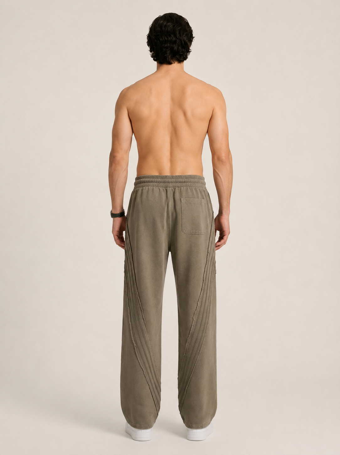 Full length backside image of a model wearing a pair of khaki sweatpants on a beige background. 
