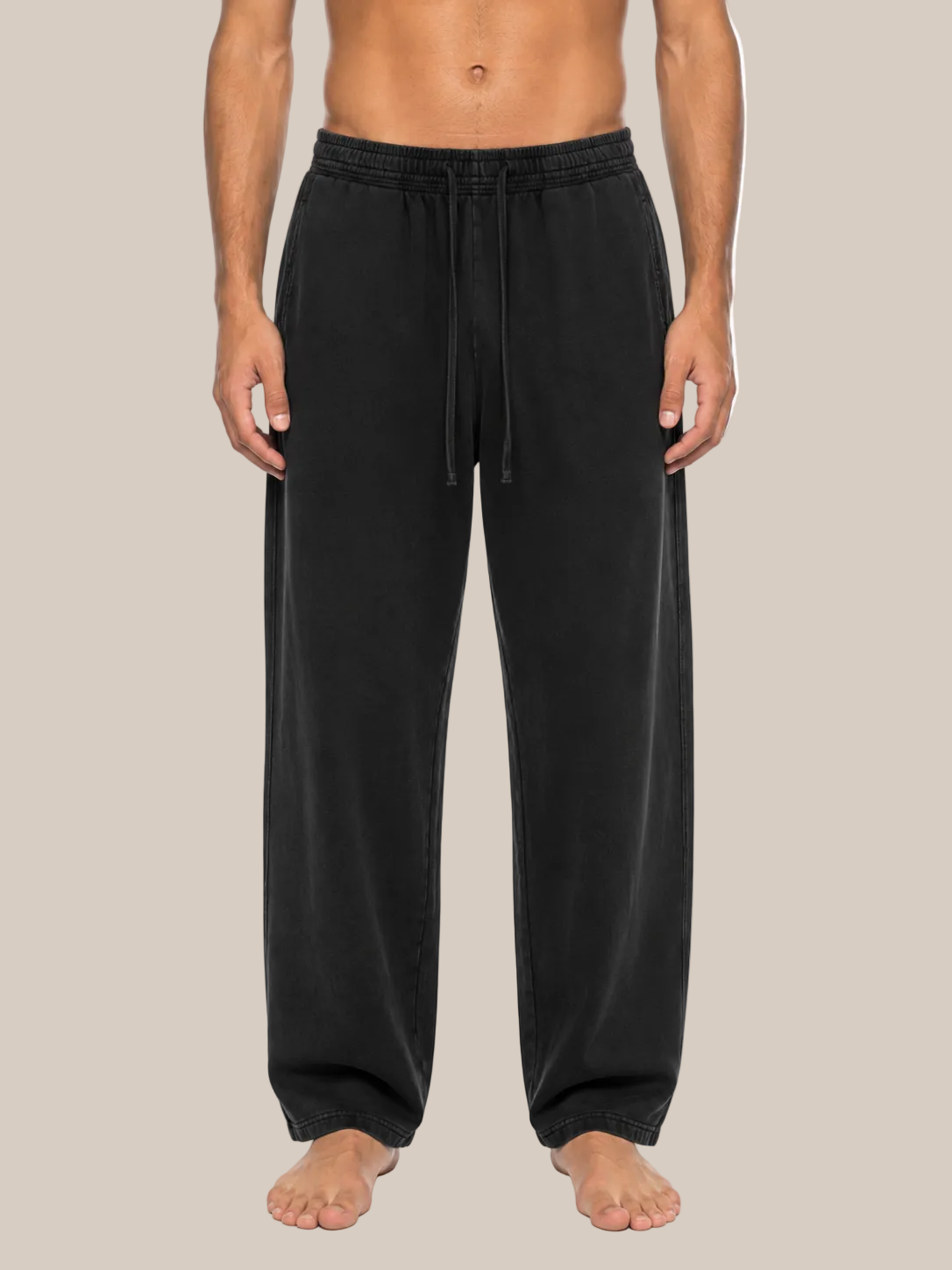 A man wearing black drawstring lounge pants, shown from the waist down against a plain beige background.