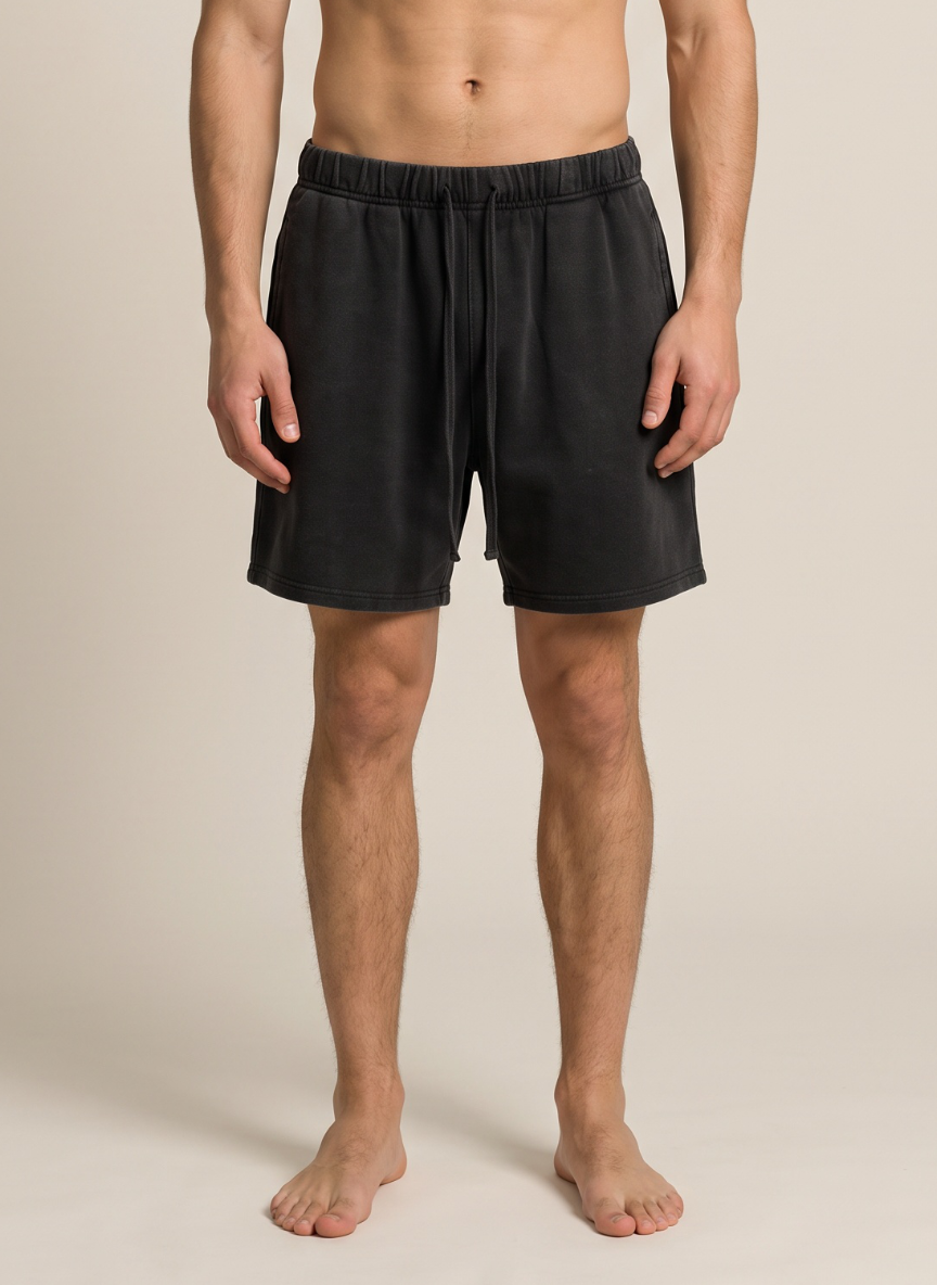 A man wearing black drawstring shorts, shown from the waist down against a plain beige studio background.