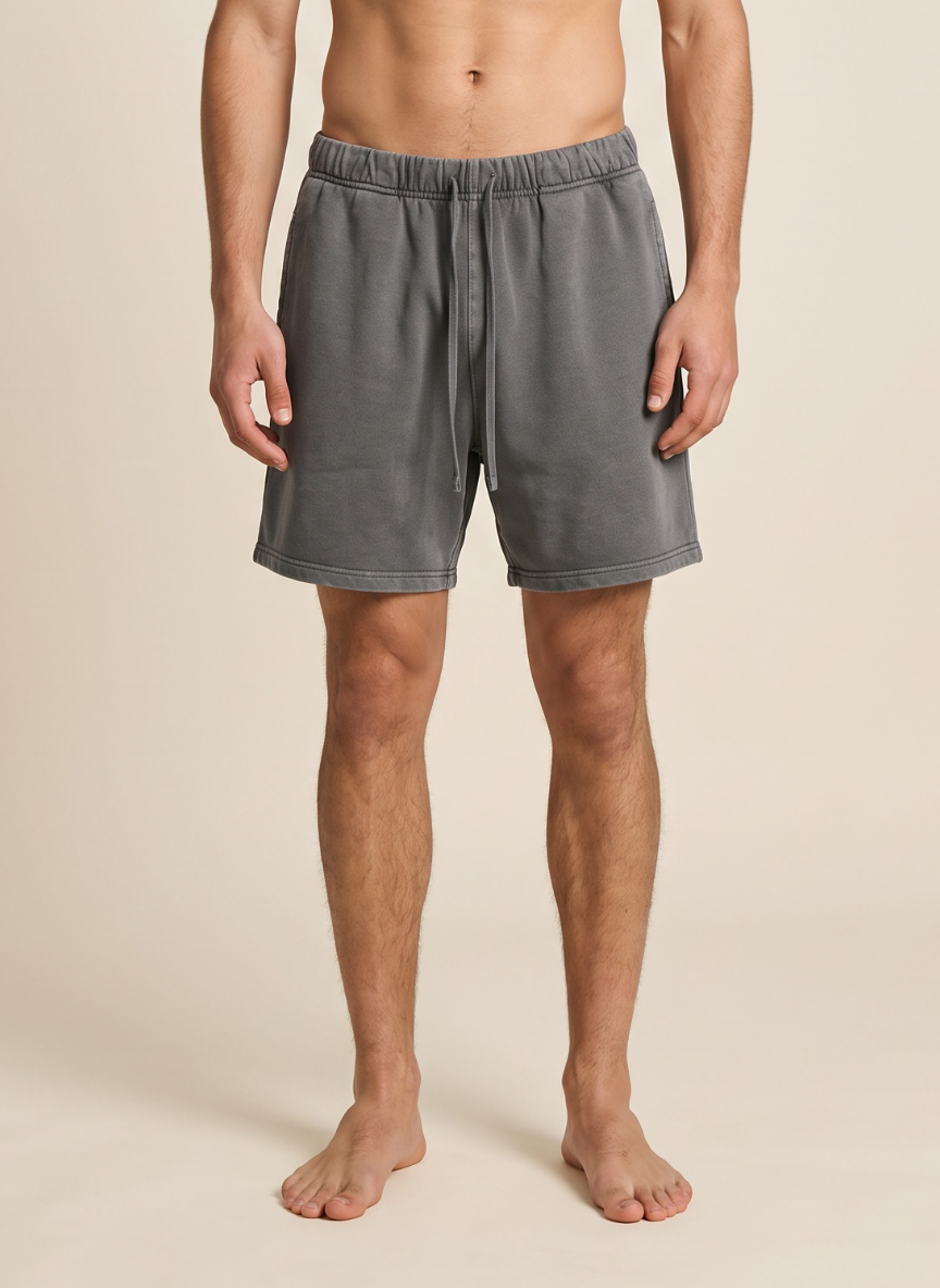 A man wearing gray drawstring lounge shorts, shown from the waist down against a plain beige studio background.