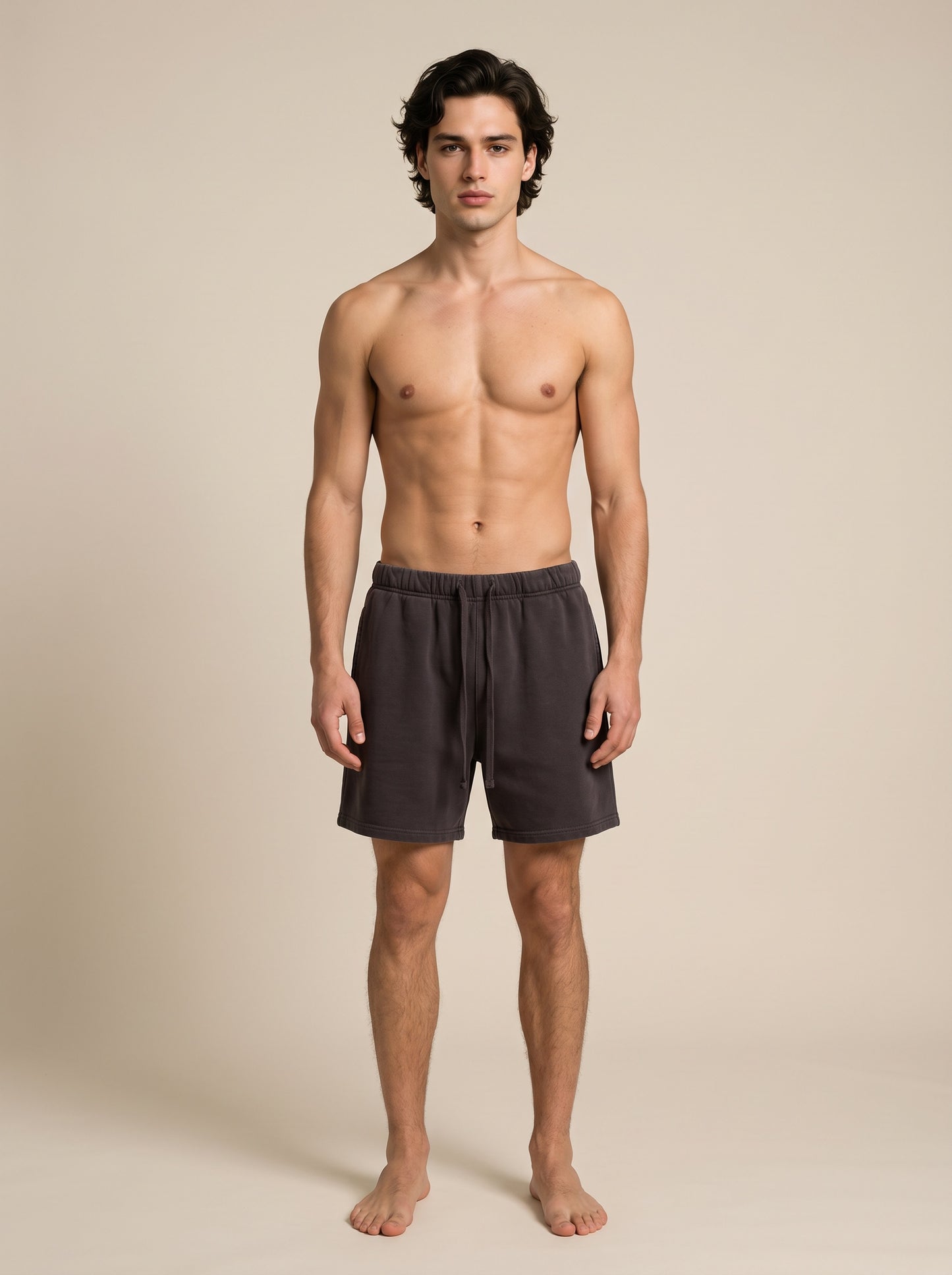 A shirtless male model stands against a plain beige studio background wearing dark purple drawstring shorts.