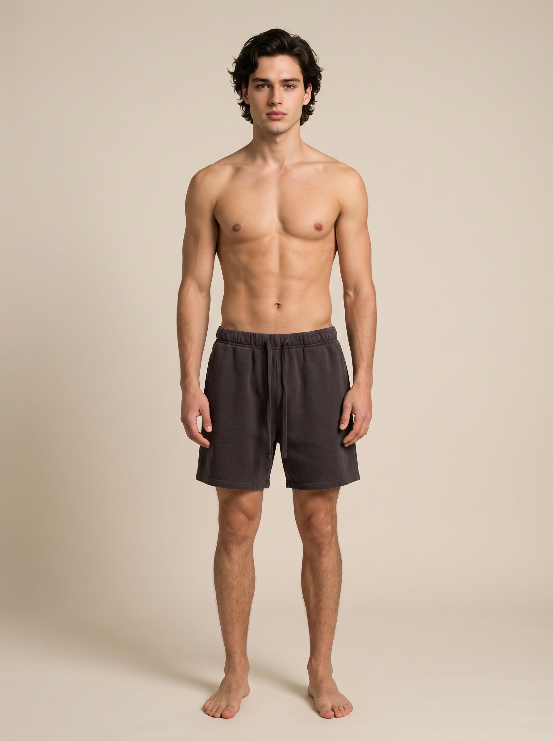 A shirtless male model stands against a plain beige studio background wearing dark purple drawstring shorts.