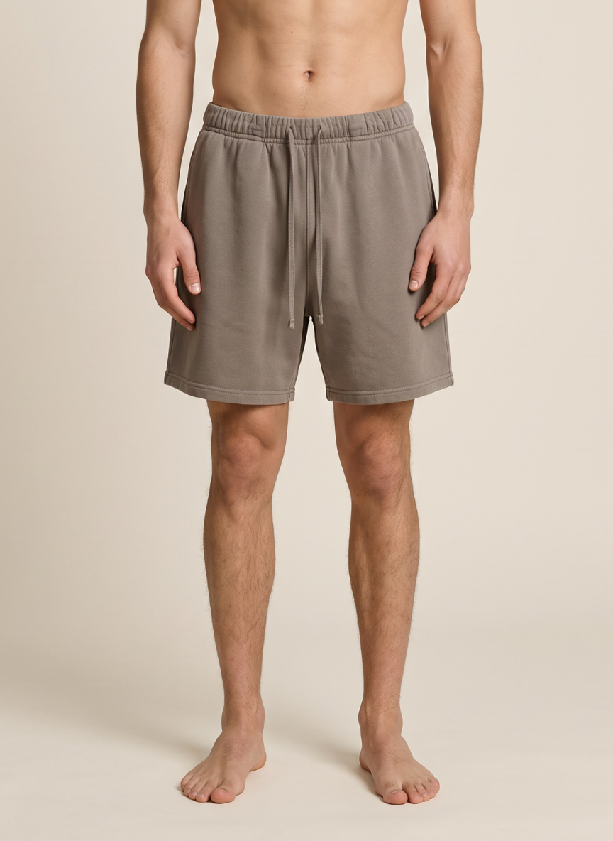 A man wearing light brown drawstring shorts, standing barefoot against a plain beige studio background.