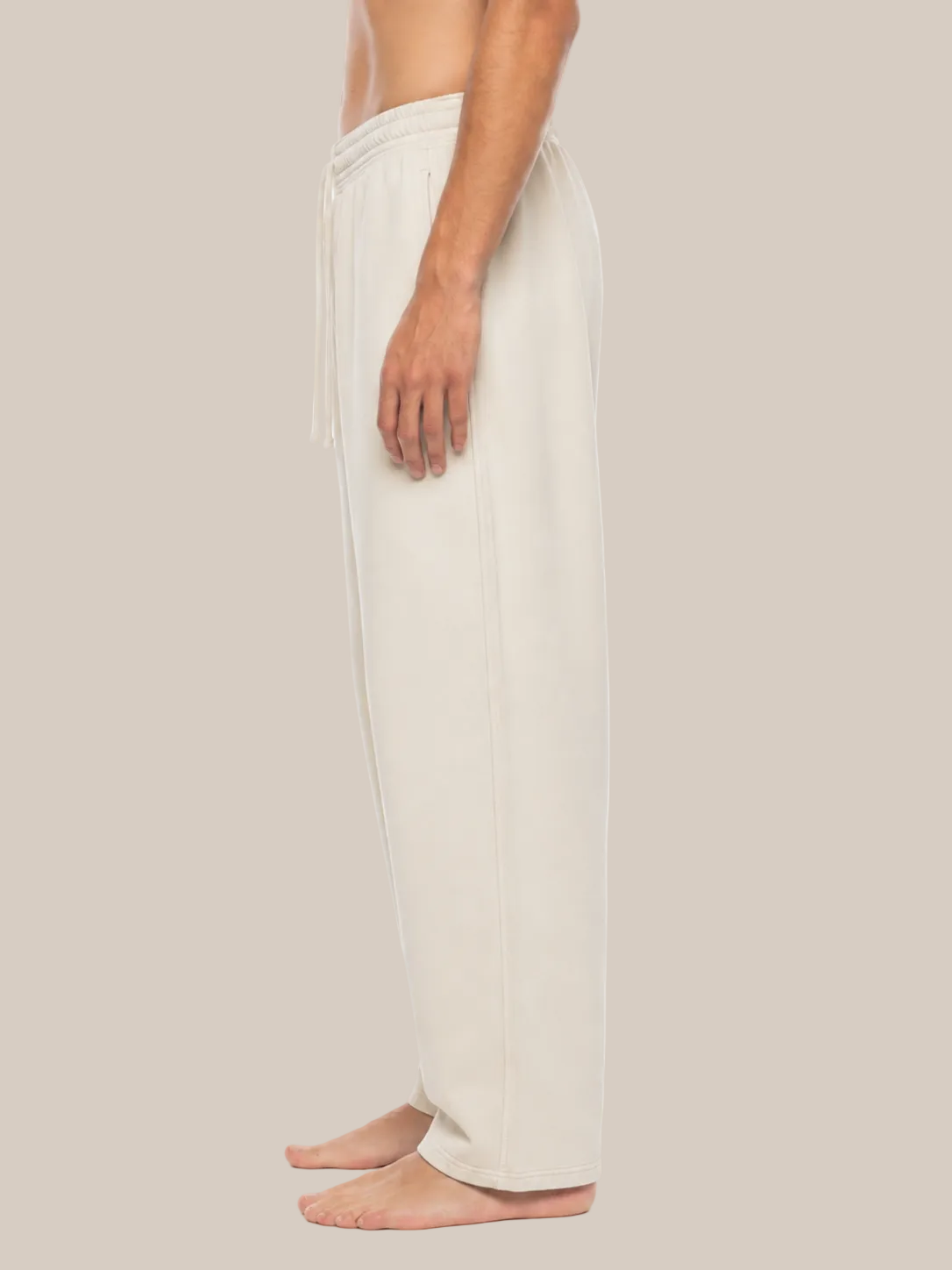 A side profile view of a person wearing light beige drawstring lounge pants against a plain white background.