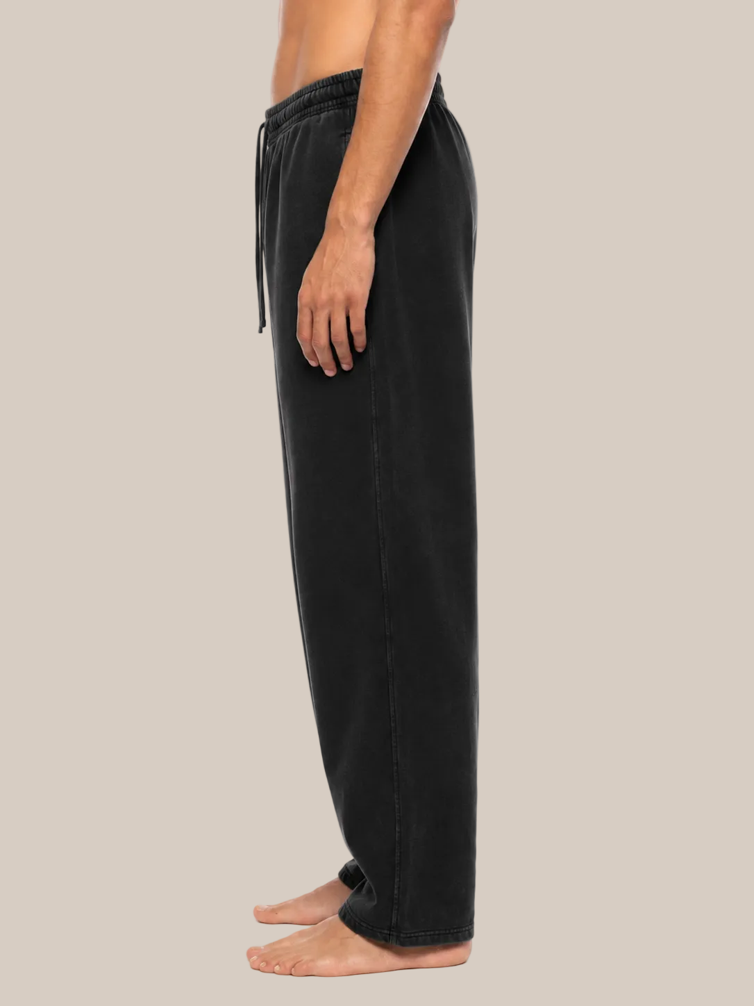 A side profile view of a person wearing black wide-leg sweatpants against a plain beige background.