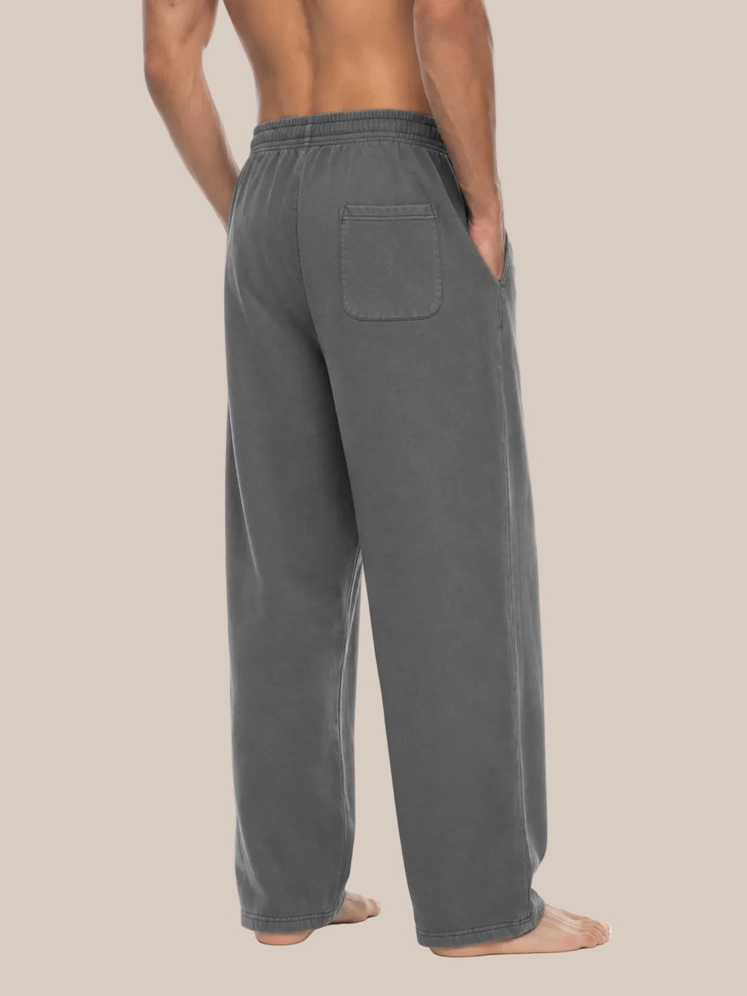 A man wearing dark gray lounge pants, shown from the back against a plain beige background.
