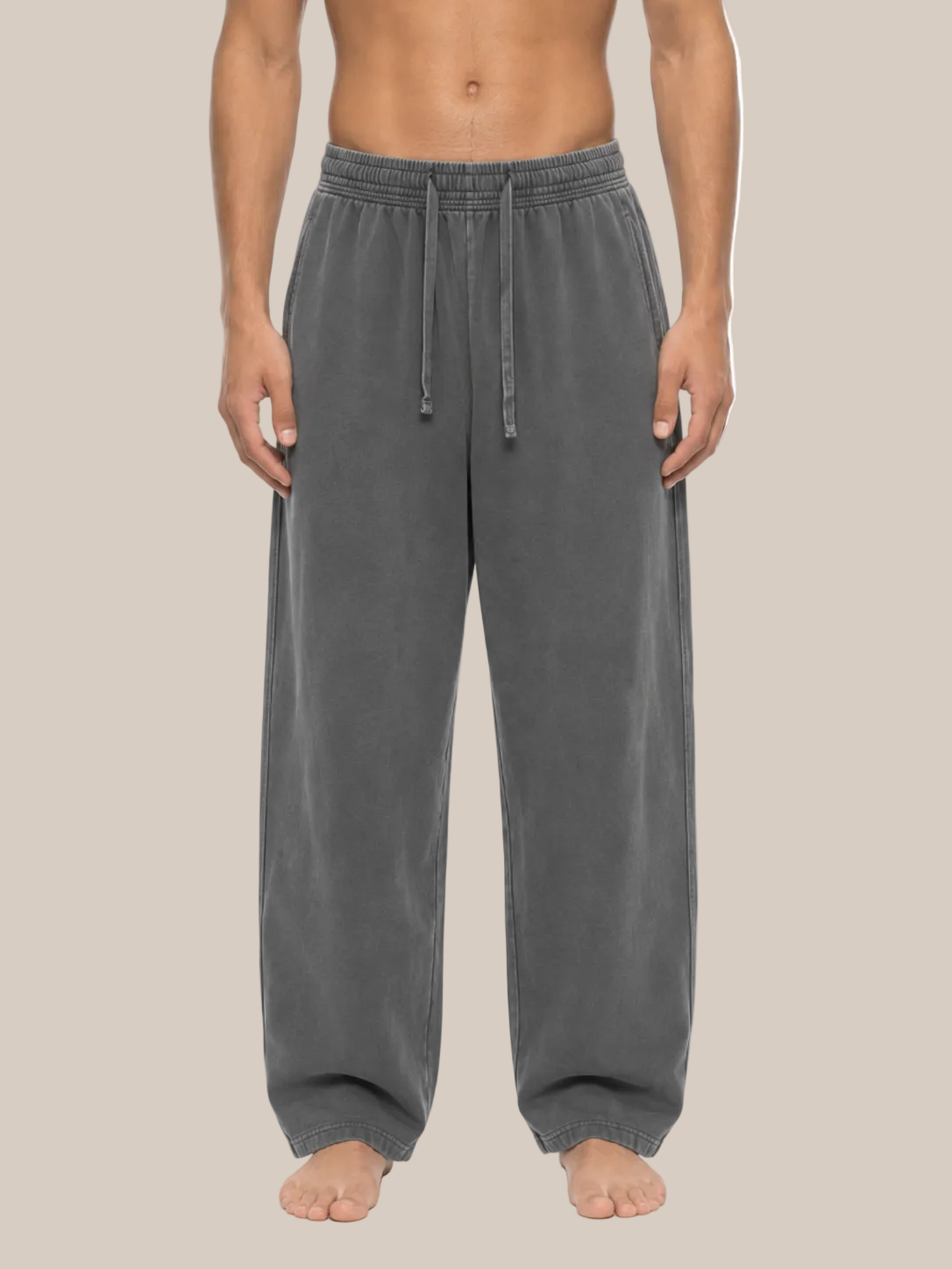 A person modeling a pair of loose, wide-leg gray sweatpants with an elastic drawstring waistband, shown against a plain beige background.