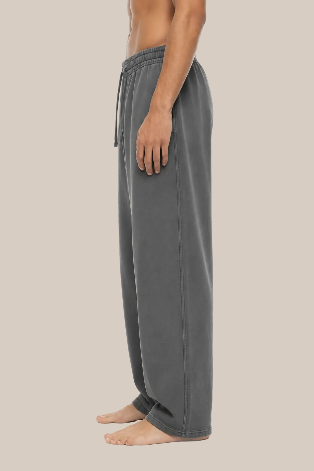 Side view of a person wearing loose gray drawstring sweatpants against a plain beige background.