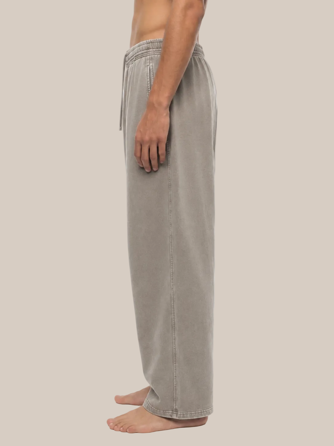 A side profile view of a person wearing light taupe wide-leg lounge pants against a plain white background.