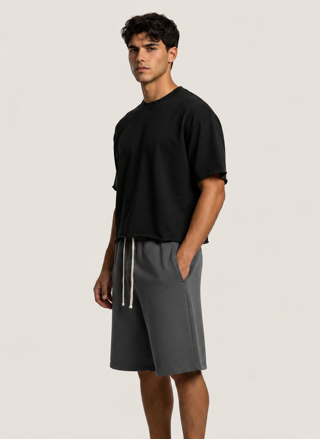 A man modeling a black short-sleeve crewneck t-shirt and dark gray drawstring shorts against a light beige studio background.